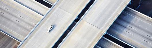 Aerial view of a single car on a multi-level highway interchange with intersecting overpasses