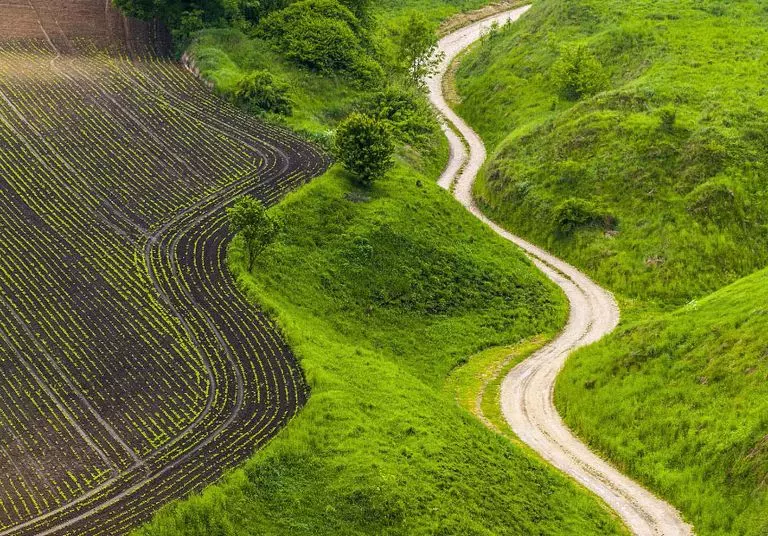 Aerial view of a double lane road cutting through a green valley surrounded by hills and trees.