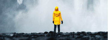 Image of a person in a yellow rain jacket standing in front of a large waterfall