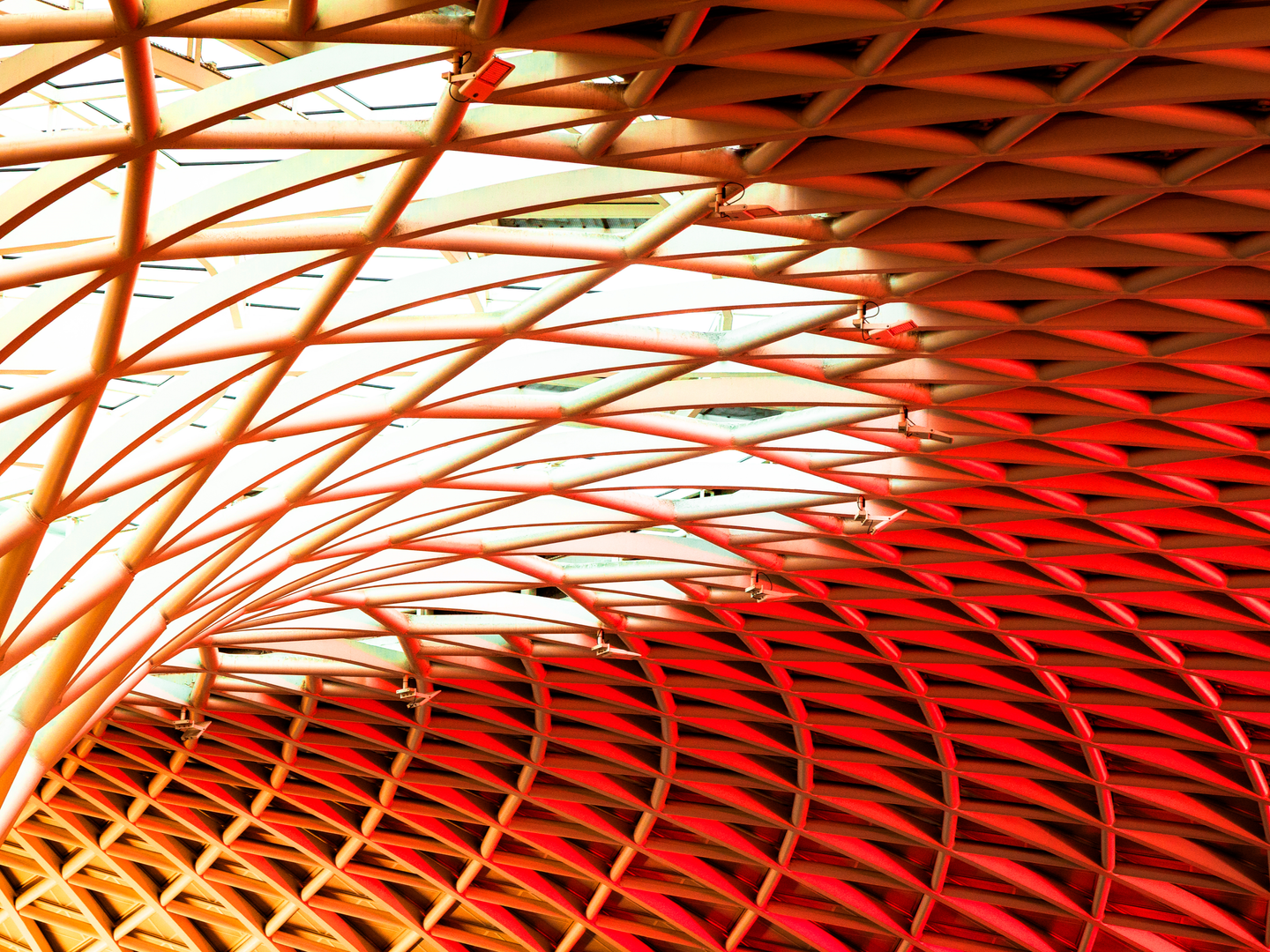 Image of curved orange and red lattice roof with bright light shining through