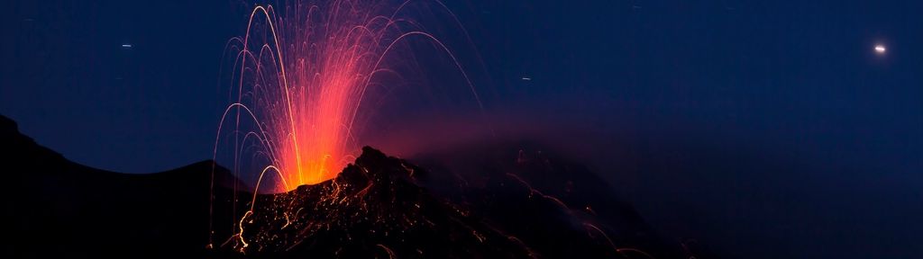 Volcanic eruption at night with glowing lava against a dark sky.