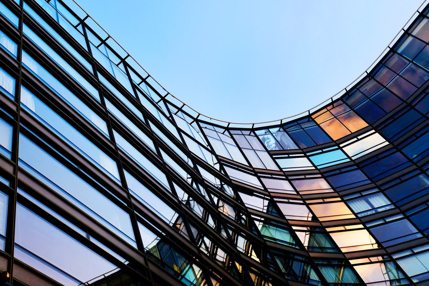 Modern curved glass building exterior with reflective windows against a blue sky