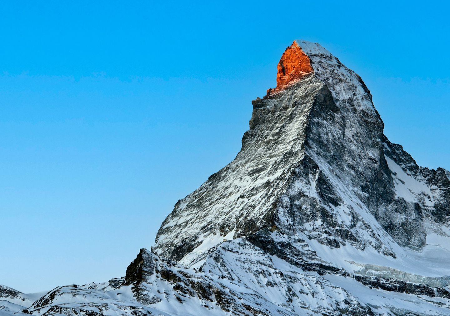 Snow-covered mountain peak illuminated by warm sunlight against a clear blue sky.