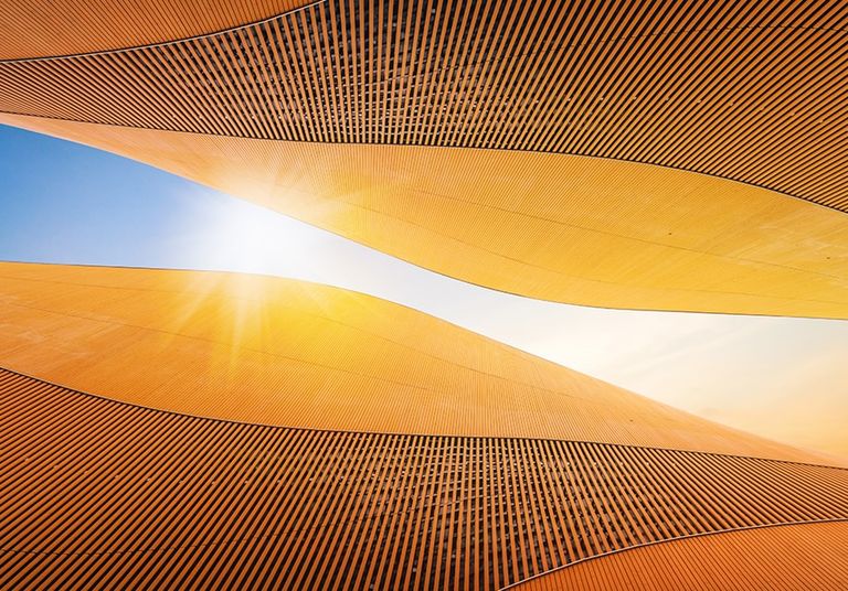 Abstract golden architectural curves with sunlight streaming through a central opening.