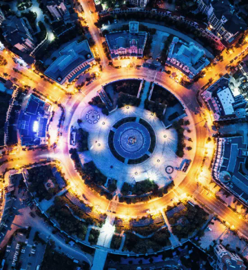 Bird's-eye view of a brightly lit circular city intersection at night, representing our research philosophy