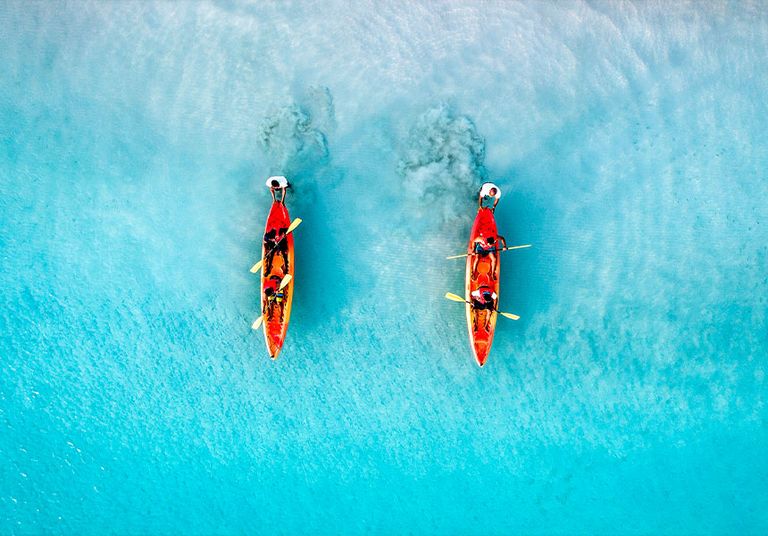 An aerial view of two orange kayaks floating on a shallow, crystal-clear ocean