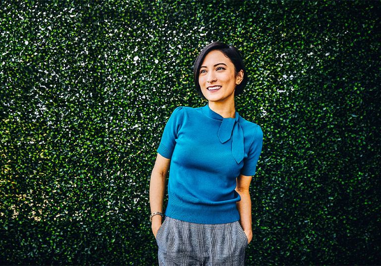 Image of a woman wearing a blue shirt against a wall covered in leaves
