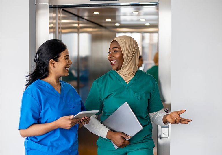 Two women in blue and green scrubs chatting with each other.