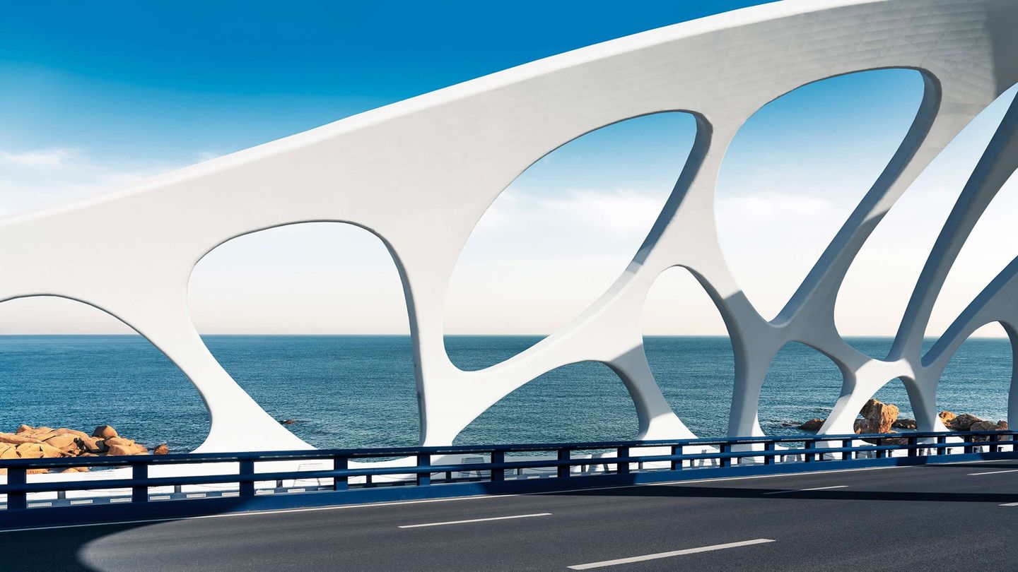 A modern bridge with white supports and a view of the ocean in the background.
