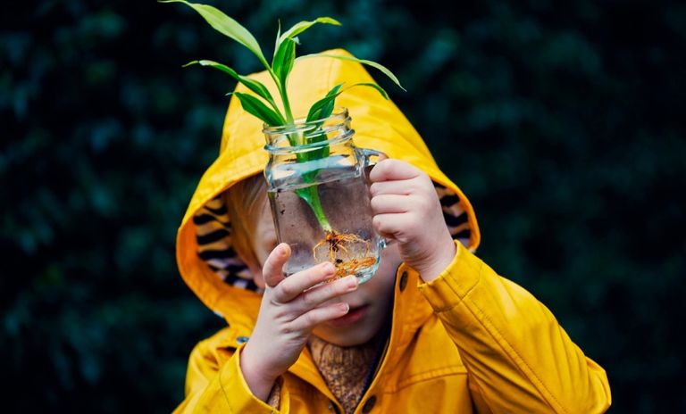 A child in a yellow raincoat holds a plant in a jar, symbolizing growth and what our clients might want in a target date strategy.  