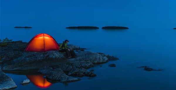 Man next to red tent gazing into a body of water