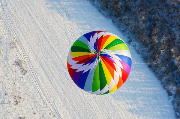 A vibrant air balloon hovering above a snowy field.