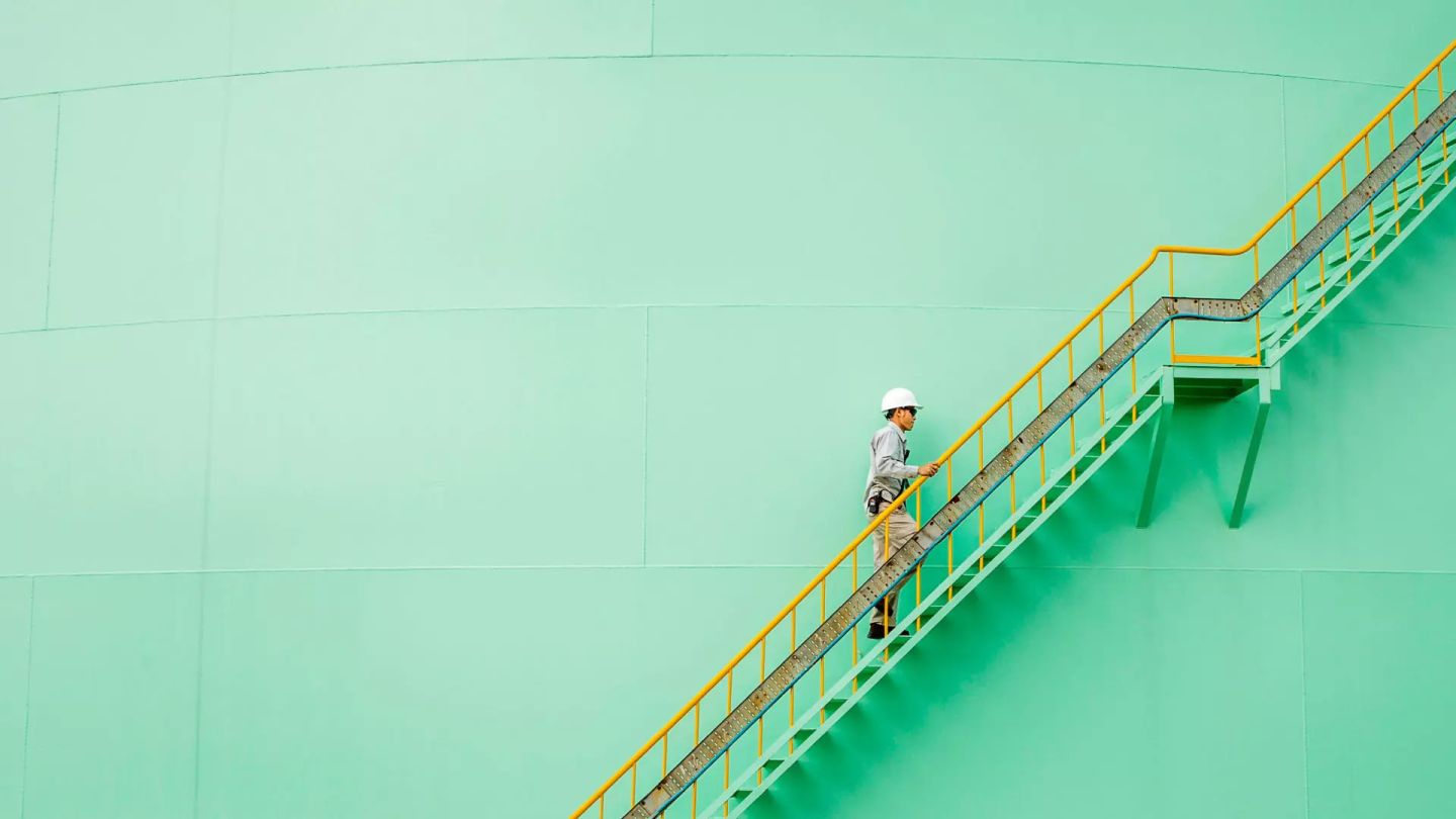 A man wearing a hardhat climbing metal stairs in an industrial setting