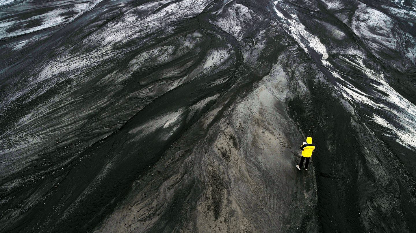 Arial view of black mountain with a man standing waring yellow jacket.
