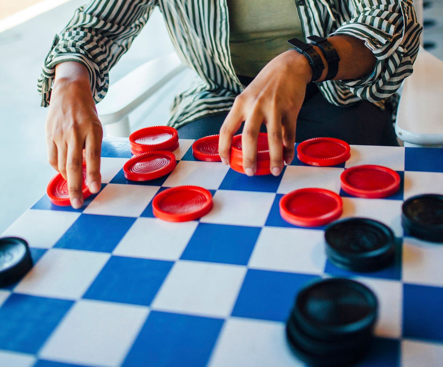 Close-up of a person’s hands moving red checkers pieces on a blue and white board.