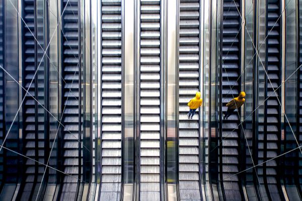 A person standing on an escalator, wearing casual yellow clothing