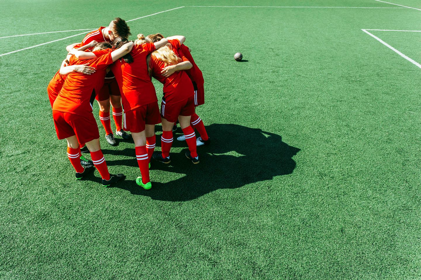 Soccer players in red uniforms huddling together on a green field before a game..